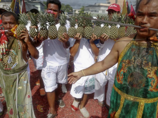 Devotee of the Chinese Bang Neow Shrine with more than ten pineapples mounted on a long spike pierced through his cheeks takes part in a procession celebrating the annual vegetarian festival in Phuket