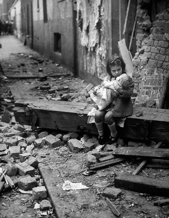 Petite fille qui se réconforte avec sa poupée sur les ruines de sa maison, Londres, 1940