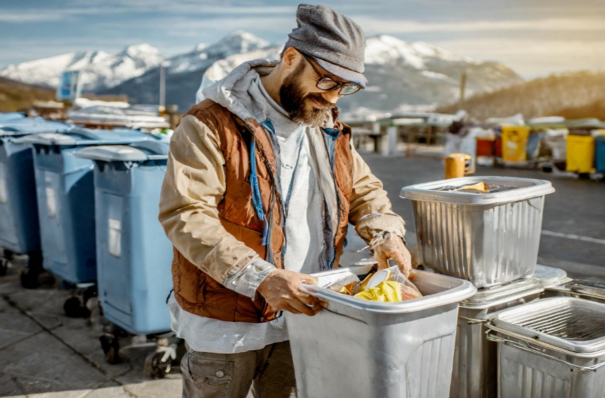 Sans abris blanc avec des vêtements usé fouillant dans les poubelles