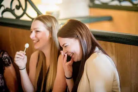 Two young women laughing joyfully while sitting indoors. Captures friendship and happiness.