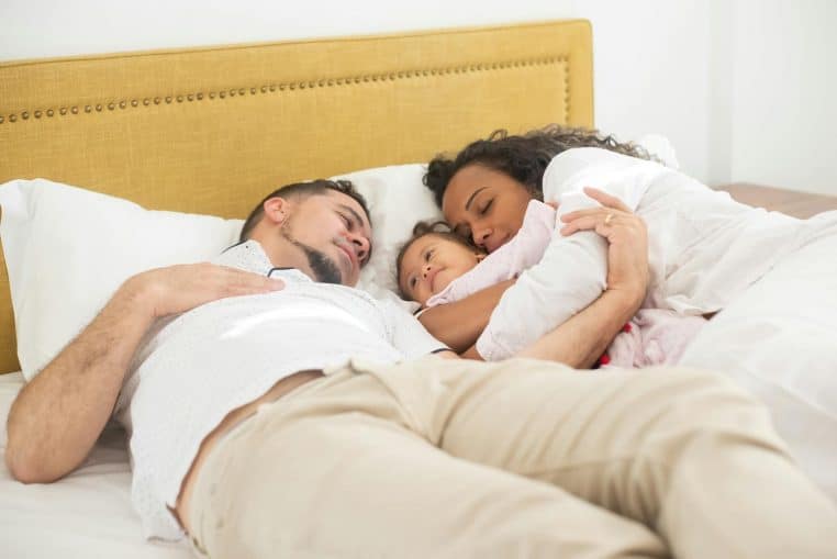 A family of three enjoying a peaceful morning cuddle in bed.