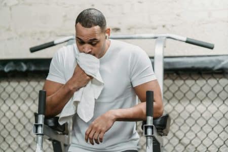 Serious African American male wiping face with towel during abdomen exercises on stand in modern gym
