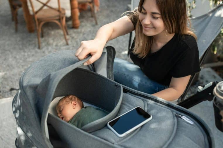 A mother joyfully gazing at her sleeping baby in a stroller, enjoying a sunny day.