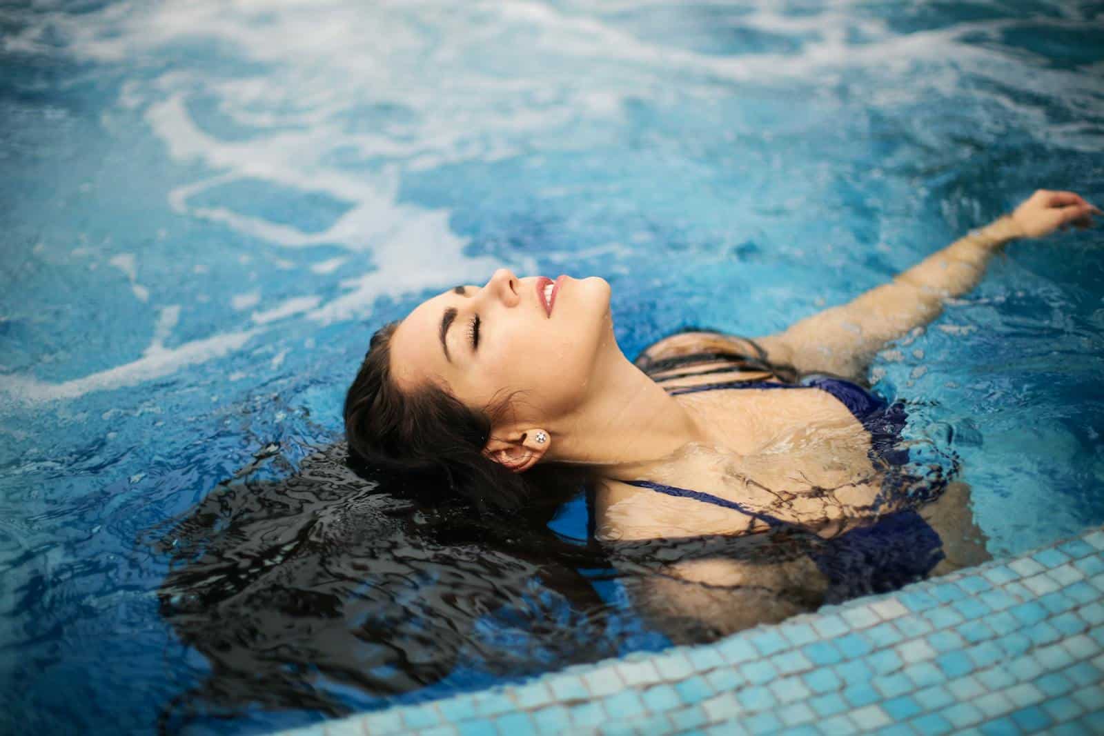 A woman enjoys a relaxing moment in a clear, blue swimming pool on a sunny day.