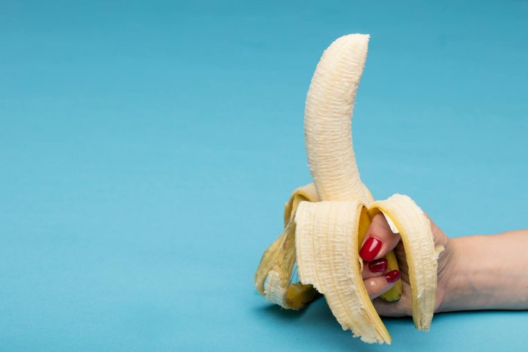 Peeled banana held by hand against a blue background, offering conceptual visual appeal.