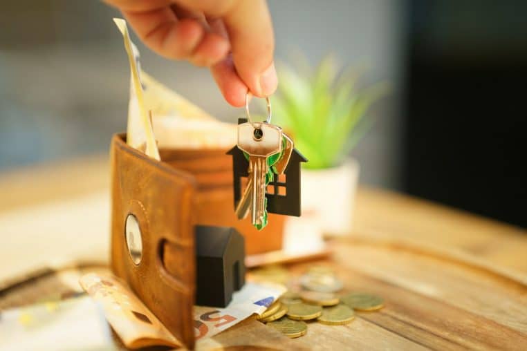 Hand holding keys with house charm and wallet.