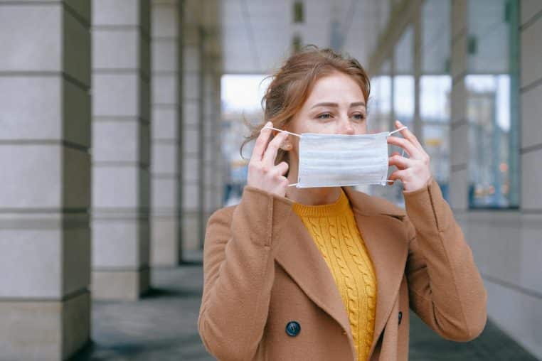 Young woman adjusting her face mask in an urban outdoor setting, promoting health safety and prevention.