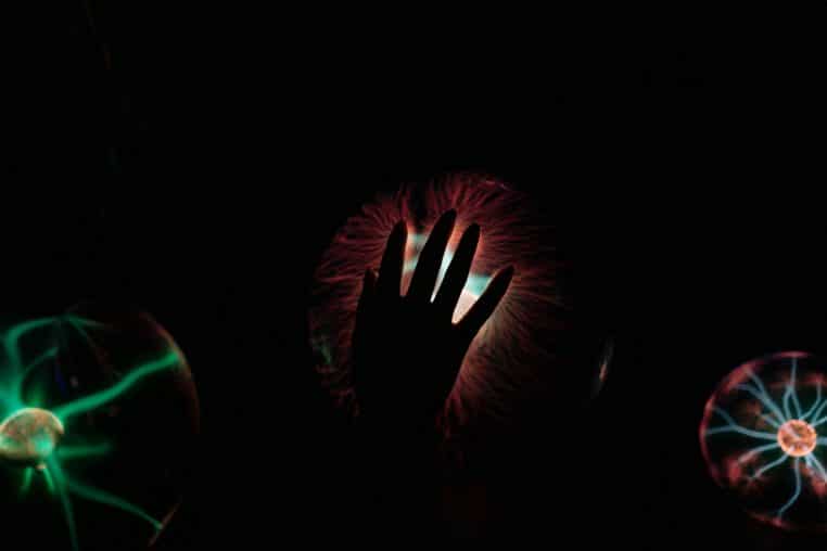 Silhouette of a hand interacting with a glowing plasma ball, illustrating electric waves.