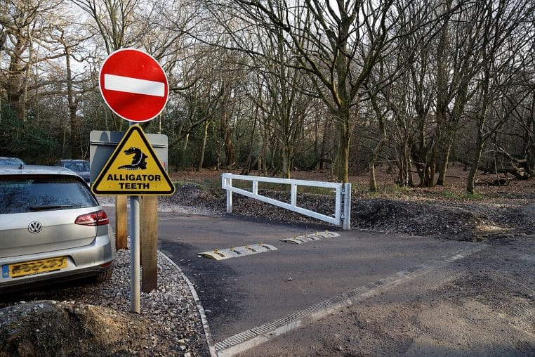barrière levante rouge et blanche ouverte sur une petite route bordée d’arbres.