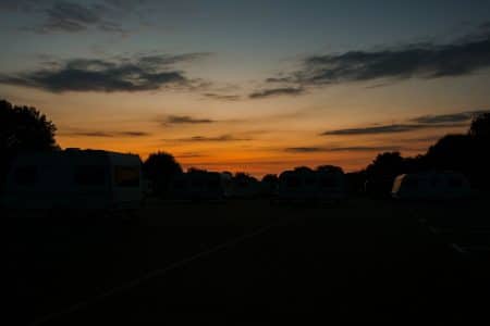 Caravanes stationnées sur un parking au crépuscule, avec le ciel teinté d’orange et de bleu.