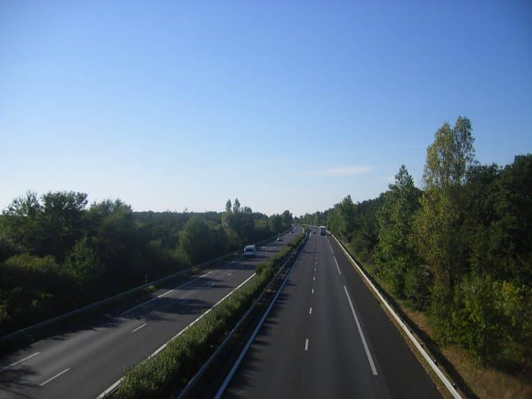 Photo d’une autoroute à deux voies encadrée de champs et de bosquets sous un ciel bleu.