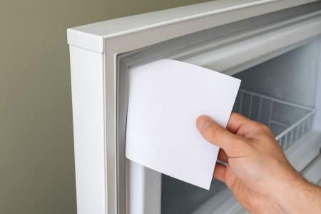 Illustration symbolique du contrôle de l’étanchéité d’un congélateur à l’aide d’une feuille A4 dans une petite fente.