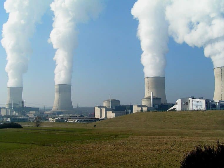 Quatre tours de refroidissement émettant de la vapeur sur un paysage vert.
