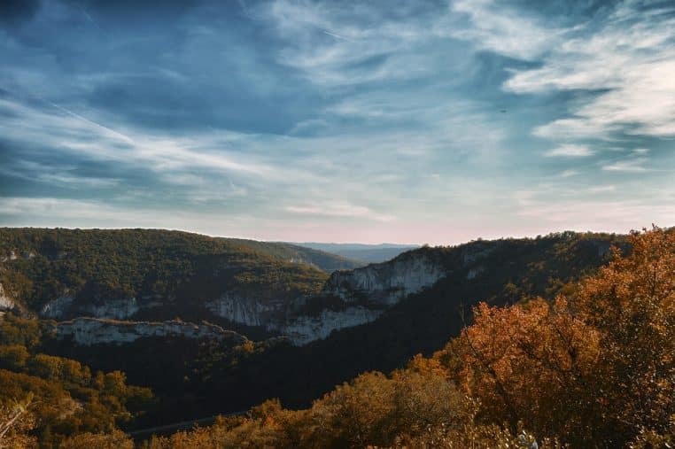 Vue panoramique d’un paysage vallonné en Aveyron sous un ciel bleu bordé de nuages.