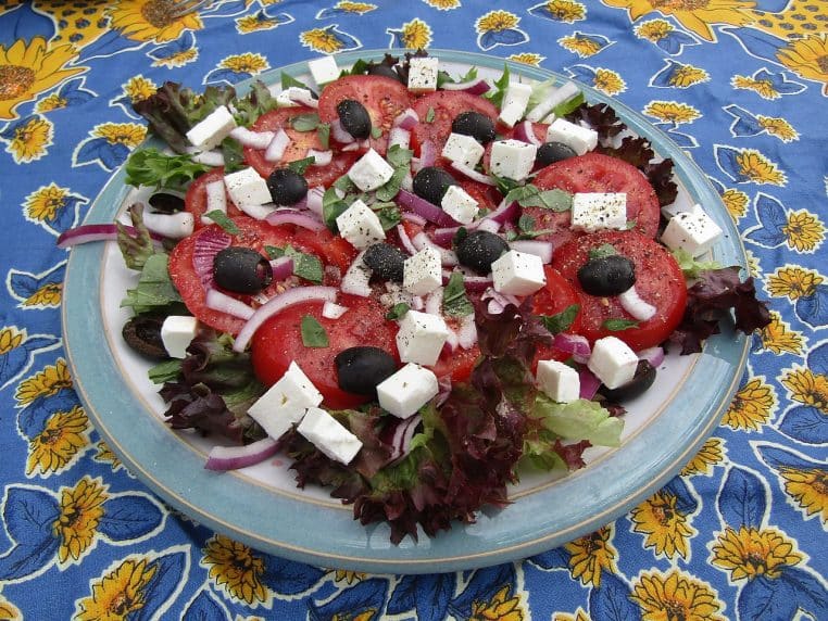 Bol de salade aux tomates, olives noires et feta, sur un fond en bois.