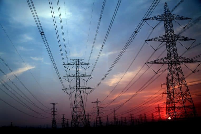 Pylônes électriques alignés sous un ciel rougeoyant.