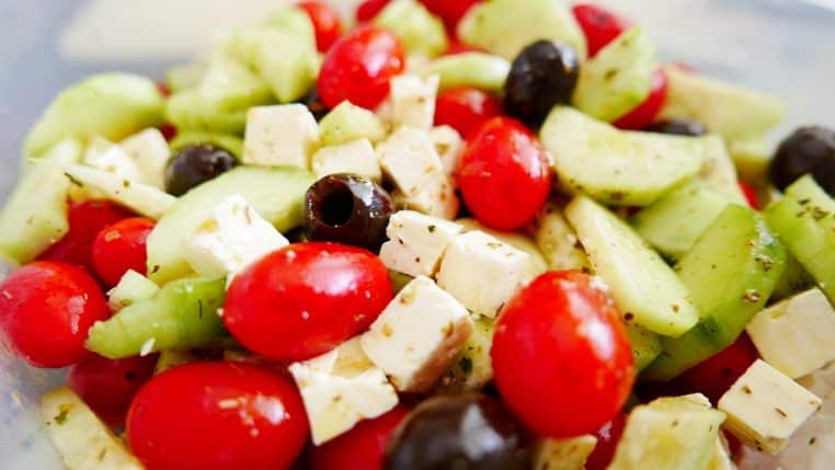 Bol de salade grecque mis en scène dans un cadre extérieur, avec feta, tomates et olives.