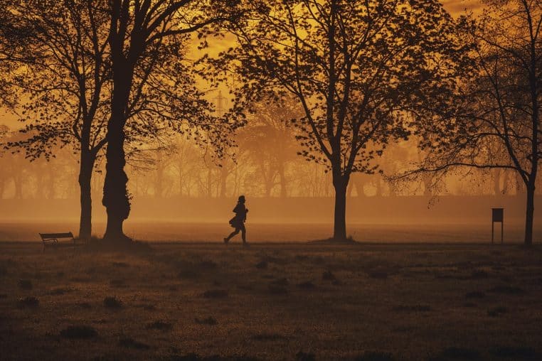 Joggeuse silhouette au petit matin dans un parc baigné d’une lumière dorée.