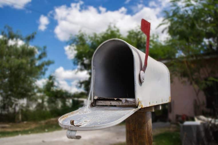 Boîte aux lettres verte ouverte dans un jardin.