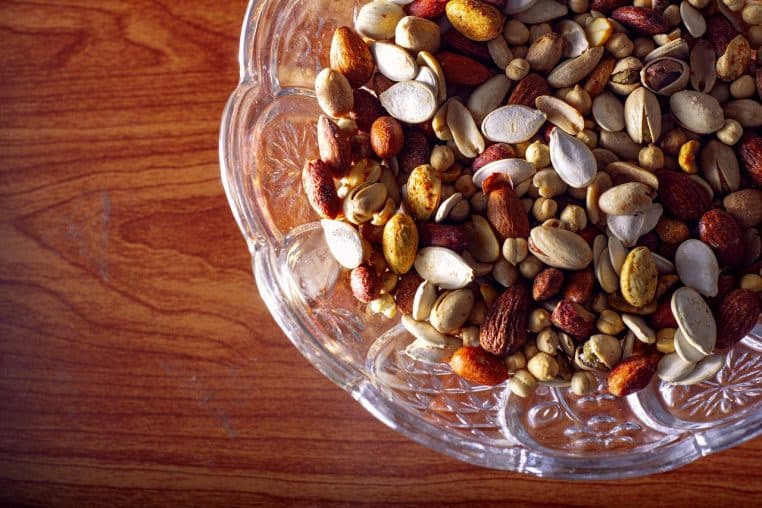 Mélange de noix, amandes et pistaches dans un bol sur fond neutre.
