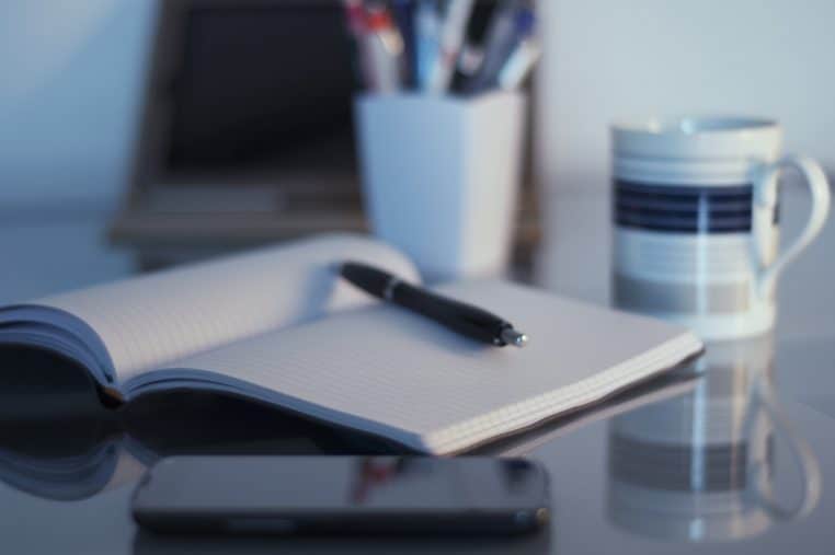 Vue d’un bureau avec ordinateur portable, cahier, stylo et tasse de café.