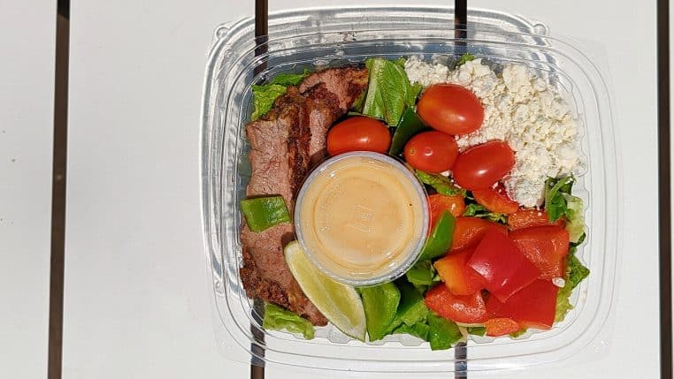 Barquette plastique contenant une salade garnie de tranches de steak.