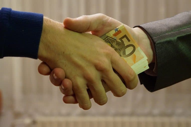 Deux mains se serrent, un billet de 50 € caché.