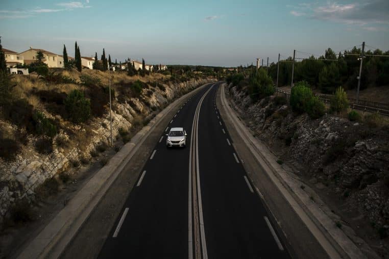 Voiture blanche sur une autoroute française bordée de vignes et de garrigue, sous un ciel clair.