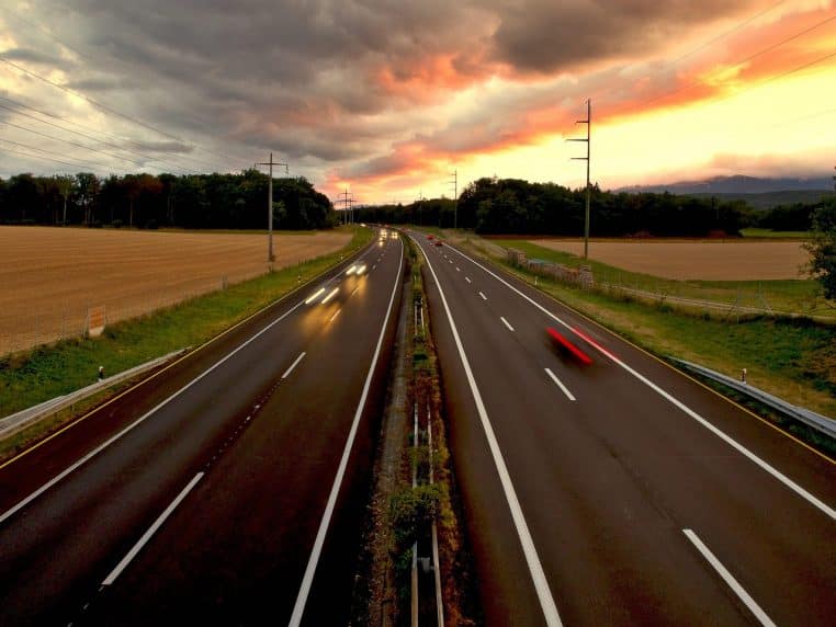 Phares flous de véhicules filant sur une autoroute sous un ciel orangé.