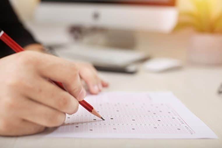 Main complétant une feuille OMR avec un crayon.