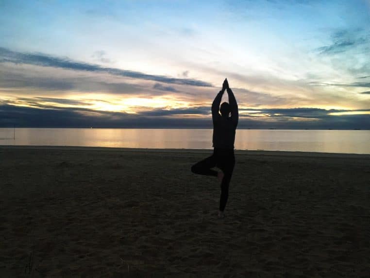 Femme en posture de yoga sur une plage au lever du soleil.