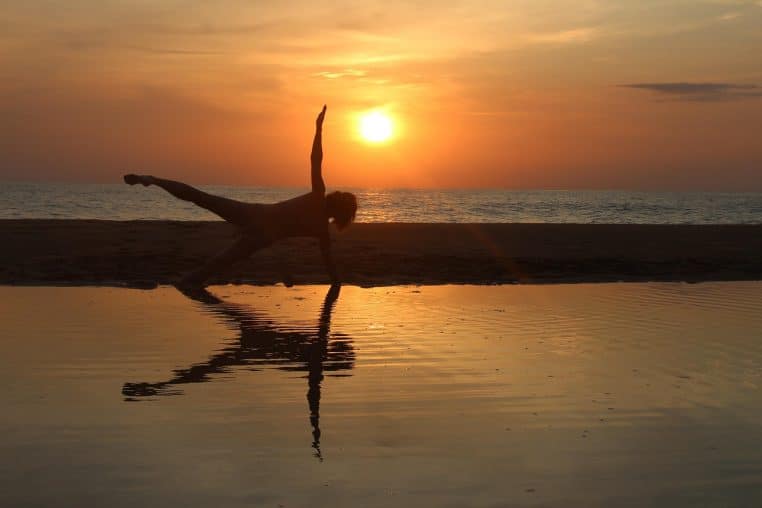 Silhouette d’une femme effectuant une posture de yoga face à un lever de soleil.