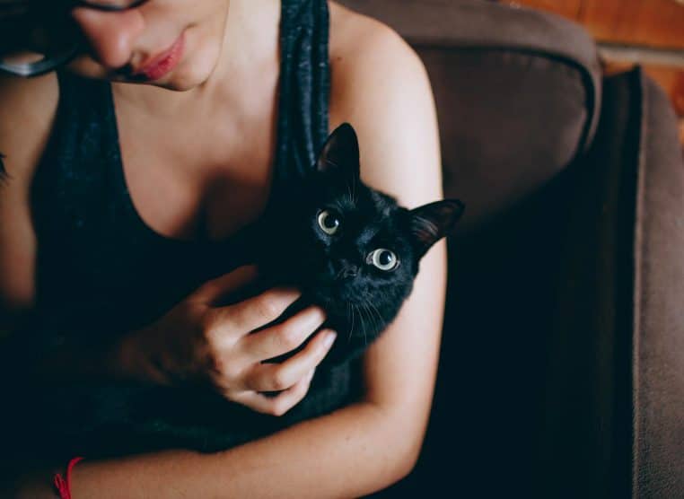 A young woman lovingly cuddles a black cat indoors, showcasing their bond.