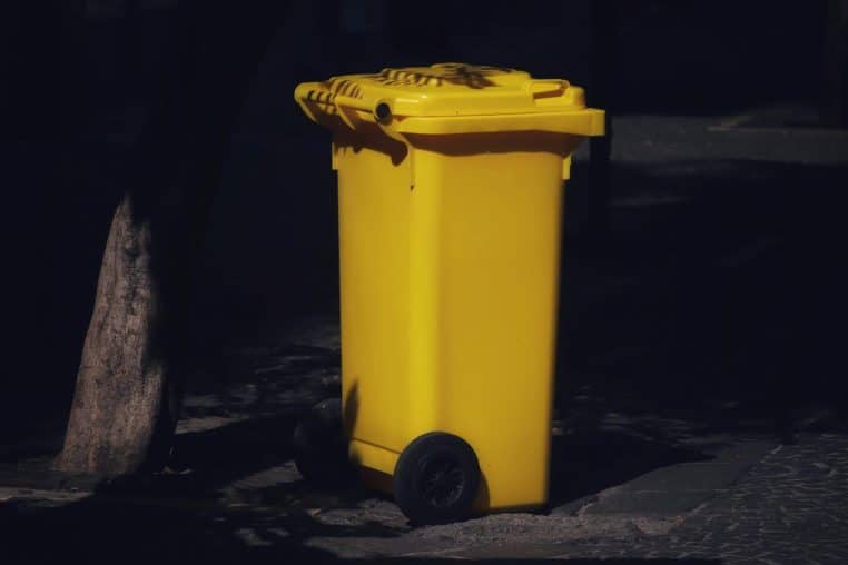 A vibrant yellow trash bin sits alone on a dark street in Salerno, Italy. Perfect for waste management themes.