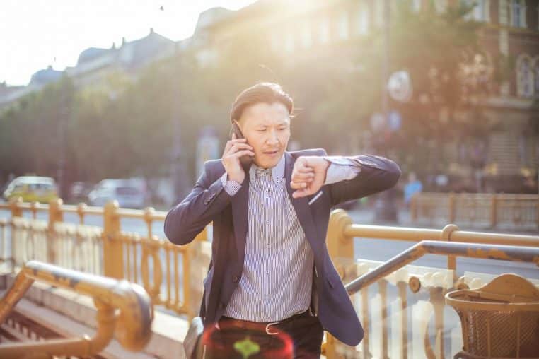 Asian businessman in suit checking time while on phone outdoors.