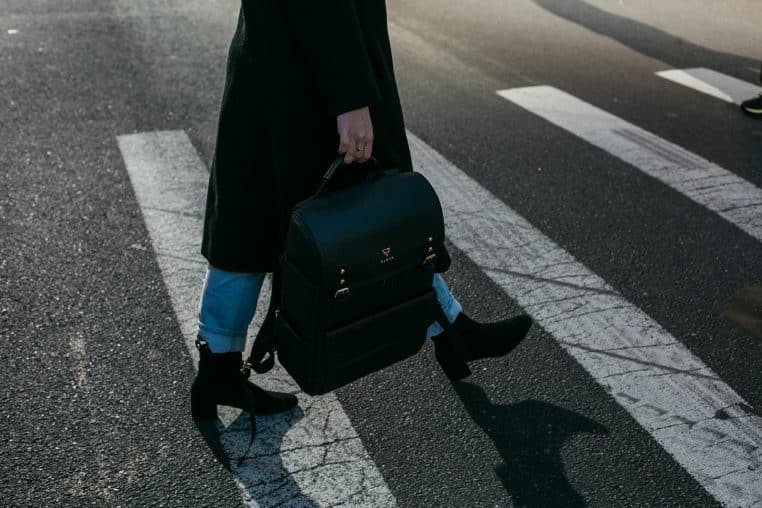 A person crosses a zebra crosswalk holding a stylish black bag in New York City.
