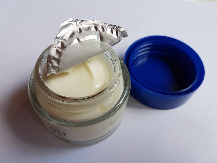 Pot de crème de jour en verre sur fond neutre.