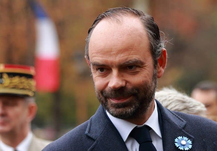 Édouard Philippe en costume sombre, levant la main pour saluer.