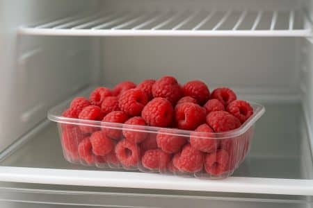 Framboises fraîches dans une barquette transparente placée sur une étagère au milieu d’un réfrigérateur.