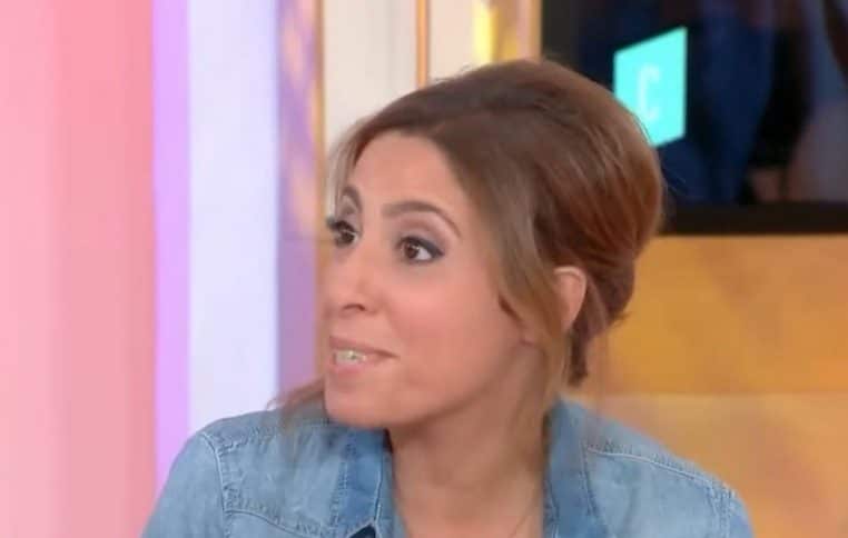 Léa Salamé, cheveux relevés, chemise en jean, réagit en plateau face à un décor rose et au logo “C