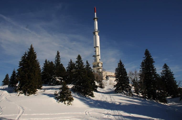 Tour de télécommunication enneigée avec montagnes en arrière-plan.