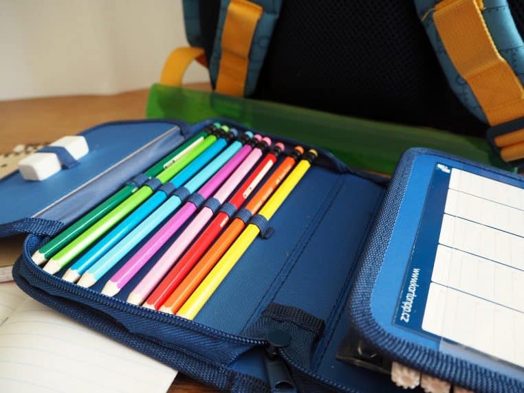 Trousse d’école bleue ouverte contenant des crayons de couleur alignés, une gomme et un cahier.