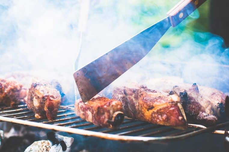 main manipulant une spatule au-dessus d’un grill fumant.