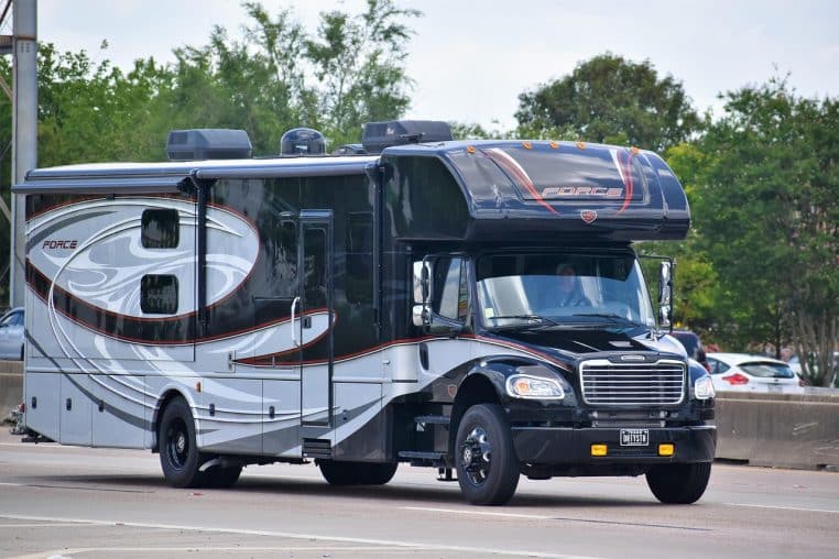 Camping-car noir sur route bordée d’arbres.