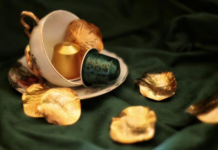 deux capsules expresso dorée et verte dans une tasse vintage sur tissu vert.