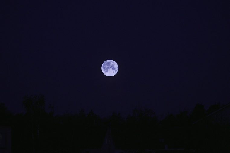 Pleine lune dominant un champ à la tombée de la nuit.