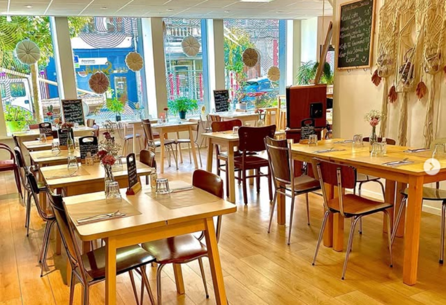 Salle lumineuse avec tables en bois, ardoises de menu et décoration végétale.