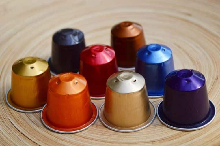 neuf capsules de café aux couleurs vives disposées en cercle sur un plateau en bois.