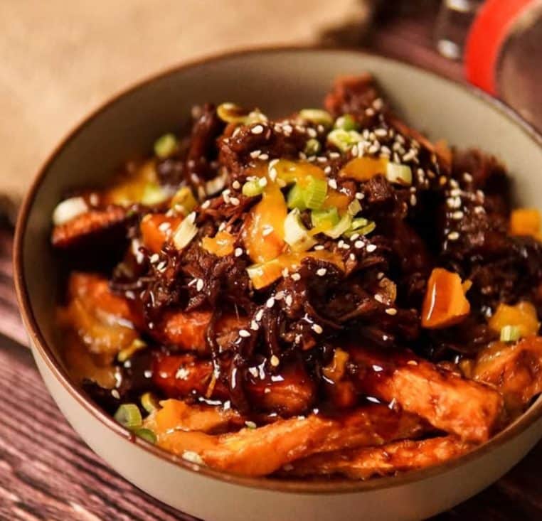 Effiloché de bœuf laqué sur frites de patate douce, sésame et cive dans un bol.