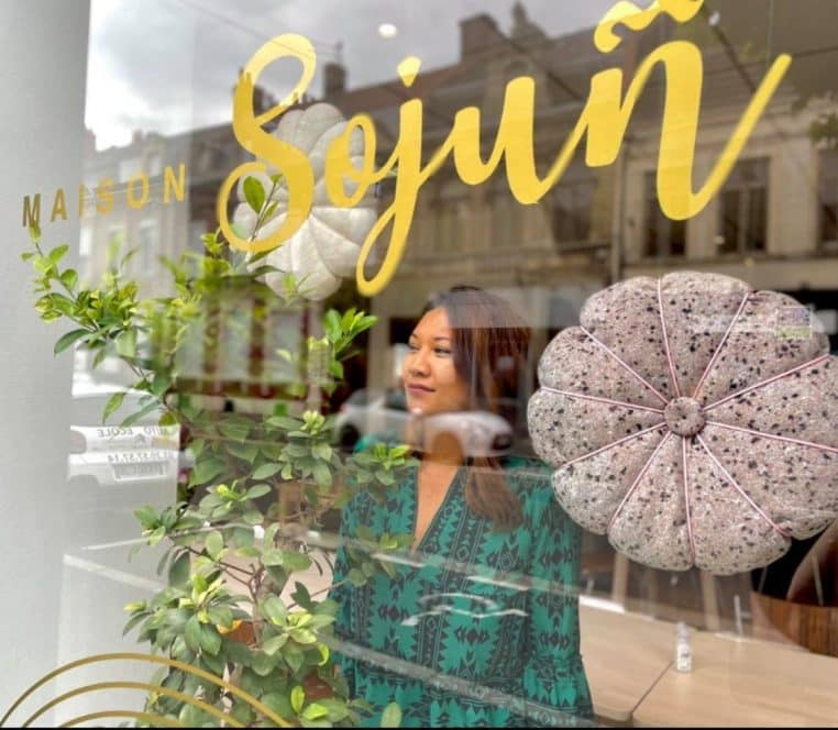 Portrait de la cheffe So’ derrière la vitrine du restaurant Maison Sojuñ.